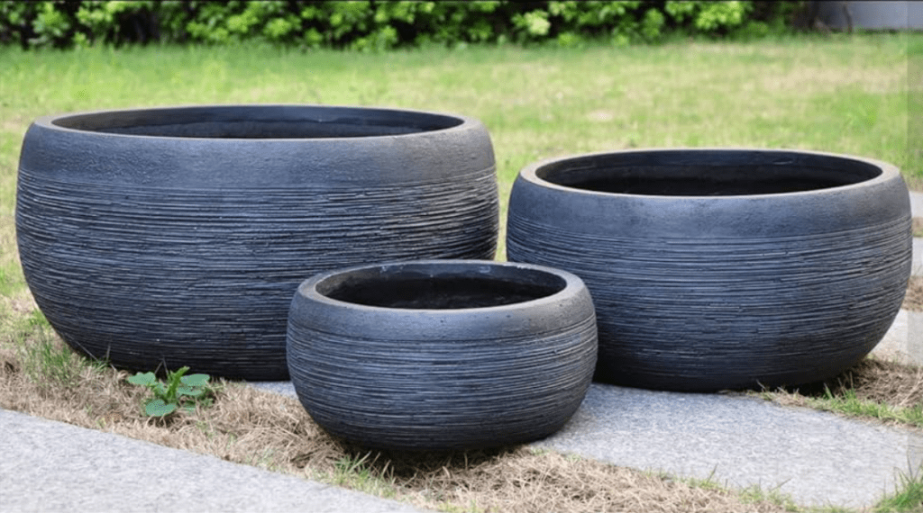 Three graduated size, black textured outdoor pots on grass and concrete.