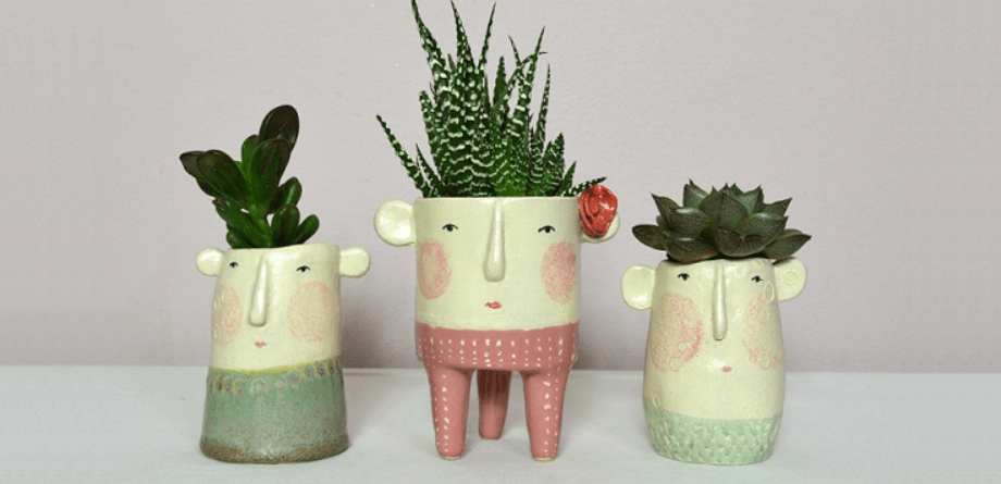 Three whimsical planters with faces and plants looking like hair.