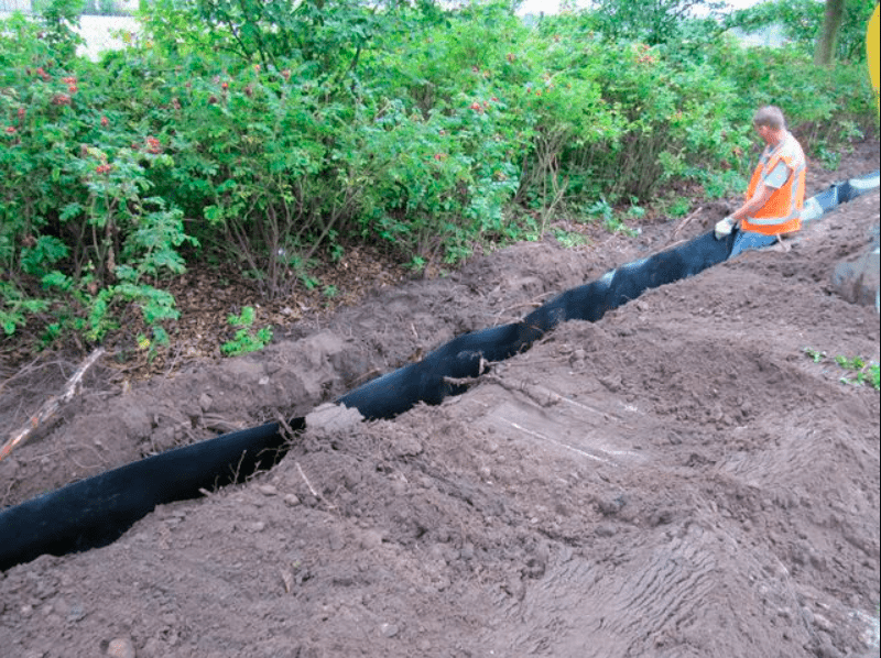 A worker installs a black silt fence in a trench for erosion control.