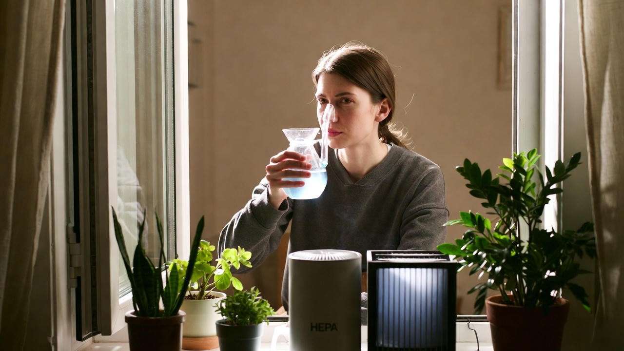 Person using a Neti pot indoors with HEPA air purifier for oak pollen allergy relief."