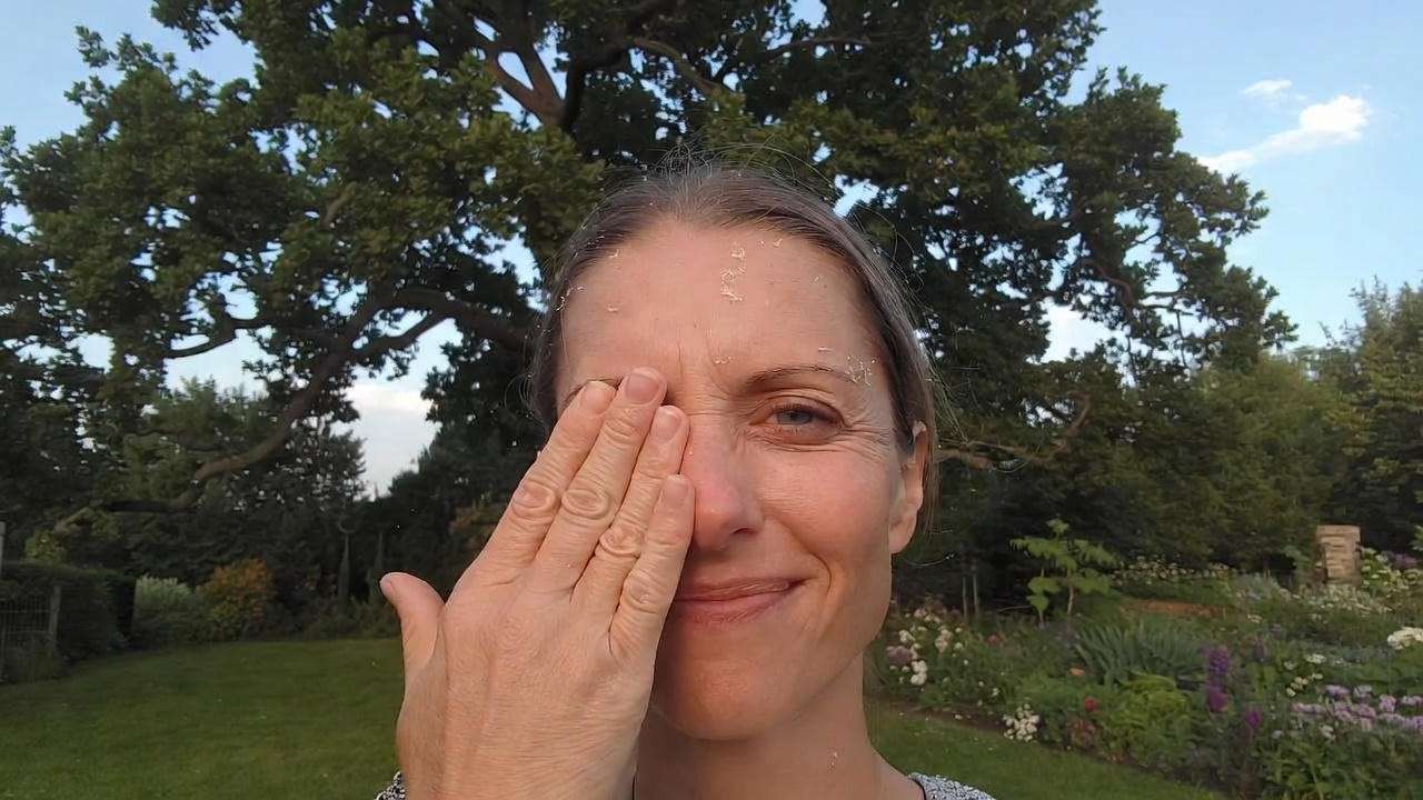 Person rubbing itchy eyes near oak tree with pollen in the air during spring."