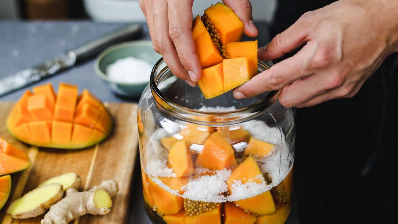 Step-by-step hands packing mango into jar for lacto-fermentation homegrown fruit process