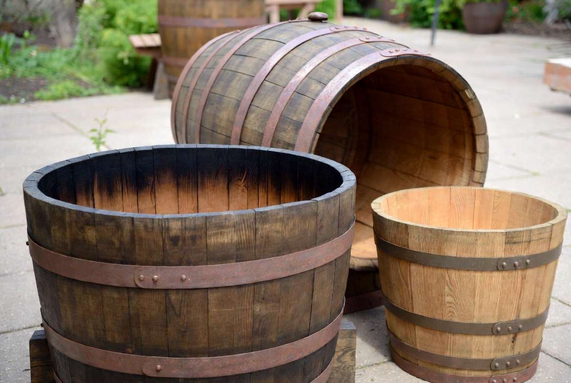 Wooden barrels for plants in various sizes and wood types on a sunny pati