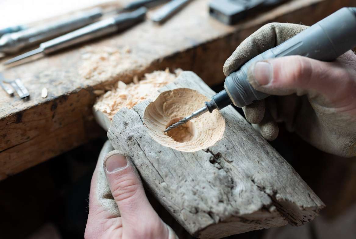 Close-up of gloved hands using a rotary carving tool to excavate a precise planting pocket into naturally weathered driftwood.