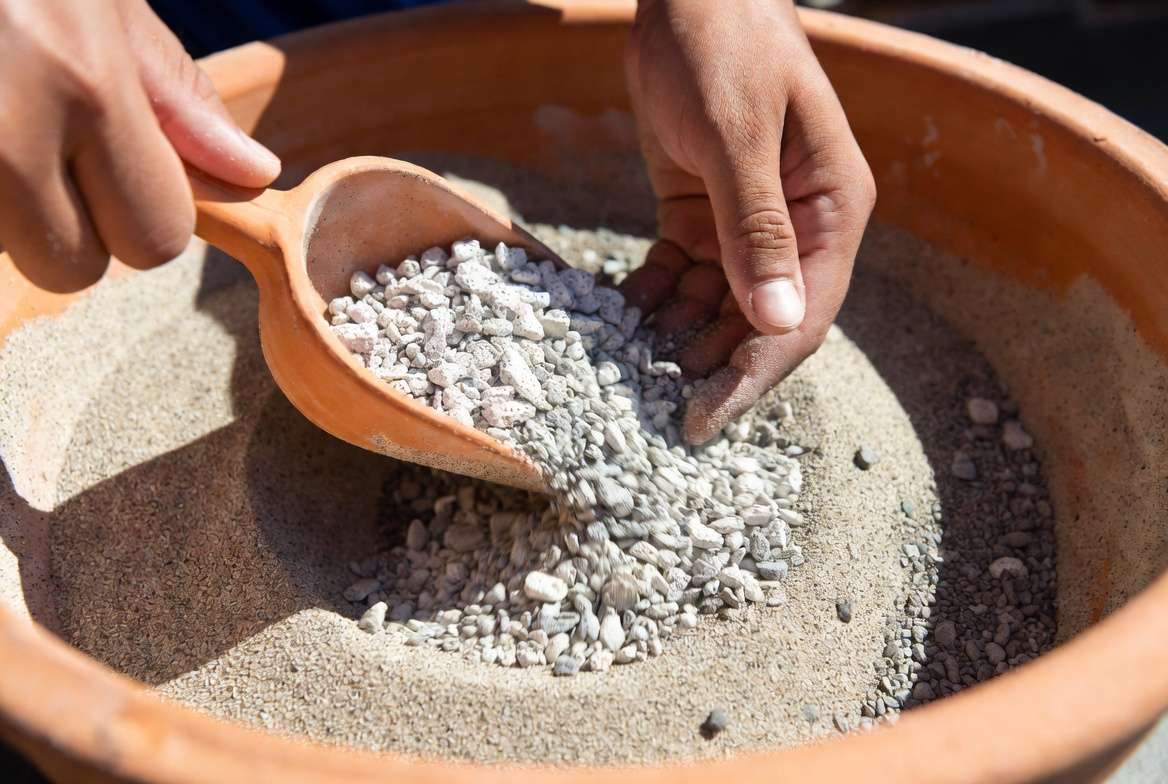 Close-up photography of a gardener mixing a high-drainage gritty soil mix for cacti, showing visible pumice, gravel, and sand components.
