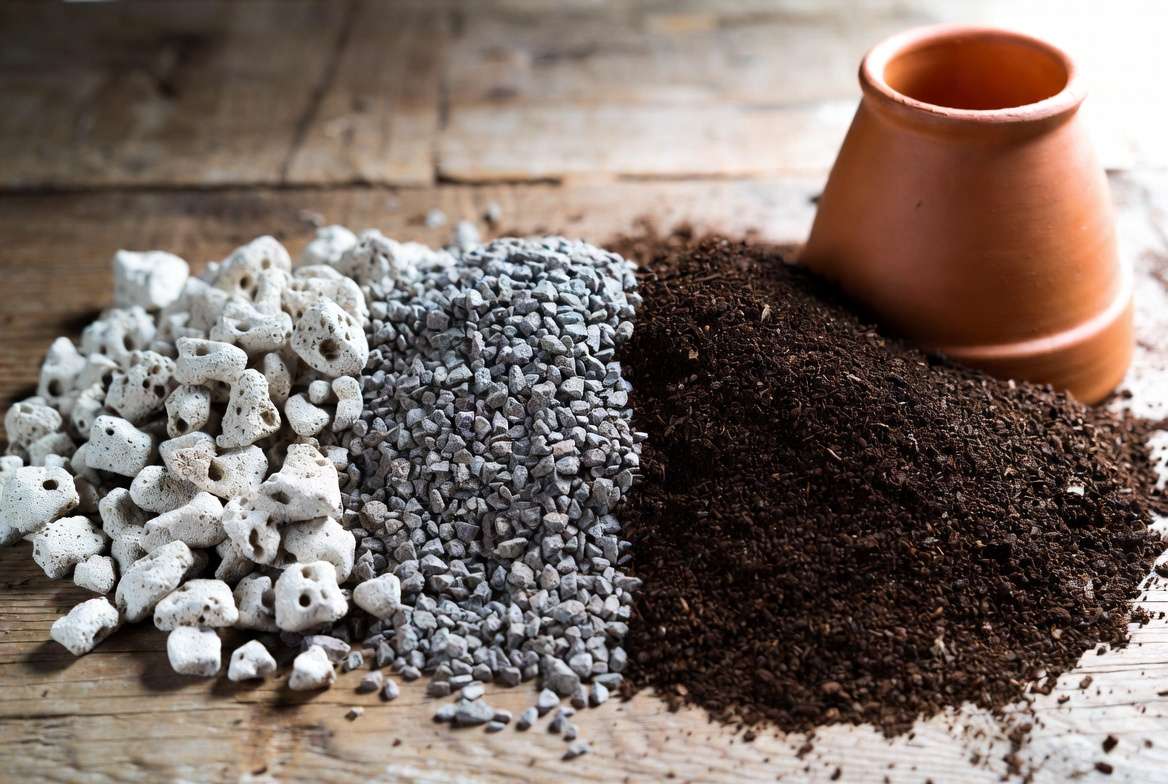 Ingredients for a gritty succulent and cactus soil mix: pumice, coarse poultry grit, and organic soil on a wooden table.